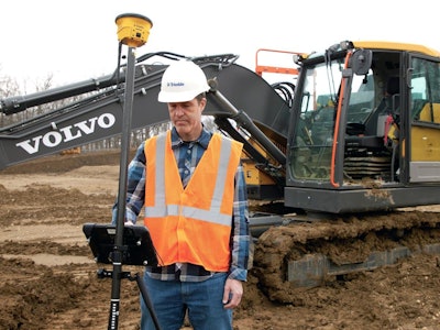 Worker in orange vest white hard uses Trimble Siteworks in front of Volvo excavator