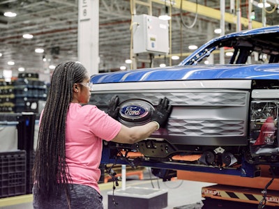 female worker places Ford emblem on grille of Ford F-150 Lightning at factory