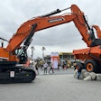 Develon DX1000LC7 excavator with bucket in back of Doosan articulated dump truck bed at ConExpo 2023