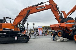Develon DX1000LC7 excavator with bucket in back of Doosan articulated dump truck bed at ConExpo 2023