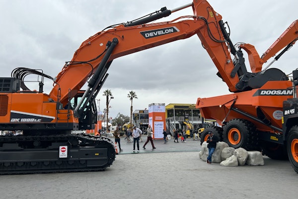 Develon DX1000LC7 excavator with bucket in back of Doosan articulated dump truck bed at ConExpo 2023