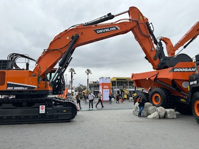 Develon DX1000LC7 excavator with bucket in back of Doosan articulated dump truck bed at ConExpo 2023