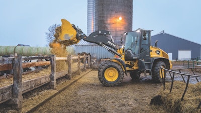 Deere 344 P-Tier compact wheel loader dumping over fence.