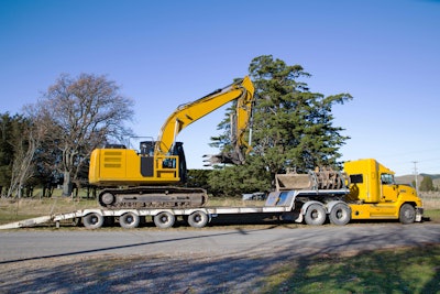 yellow excavator on lowboy trailer hauled by yellow tractor