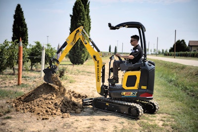 new holland E15X electric compact excavator digging in dirt beside road