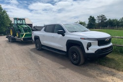 white 2024 Chevy Silverado EV Work Truck hauling John Deere tractor
