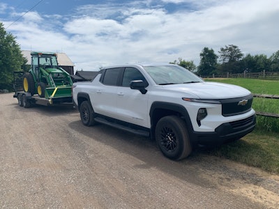 white 2024 Chevy Silverado EV Work Truck hauling John Deere tractor