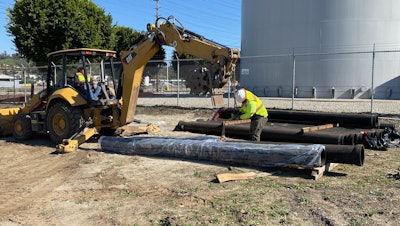 crew hooking pipe section to backhoe