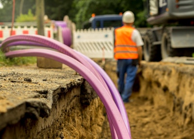 purple conduit for fiber optic line in trench with worker background