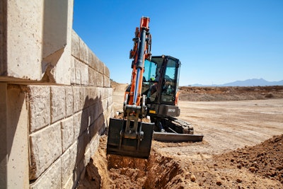 Develon DX42-7 compact excavator digging beside wall