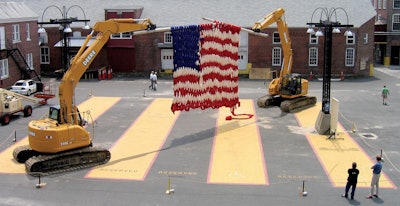 Two excavators holding giant knitted flag