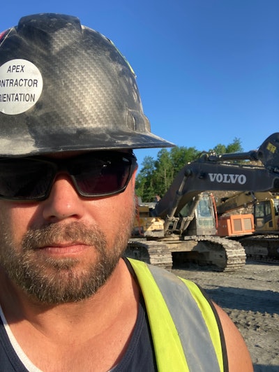 operator Brandon Balwanz wearing black hard hat in front of Volvo excavator front