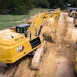 Cat 352 excavator digging trench beside dump truck