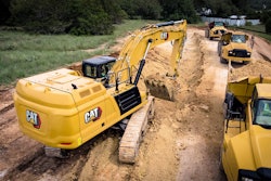Cat 352 excavator digging trench beside dump truck