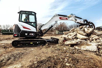 Bobcat E48 compact excavator picking up concrete debris with tine grapple
