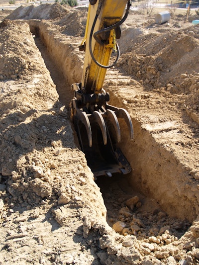 Trench being dug in dirt with excavator bucket