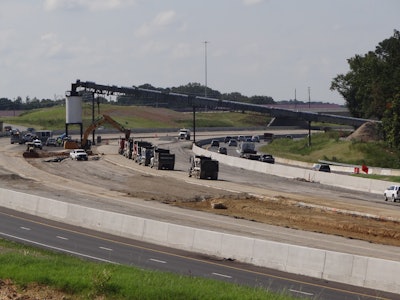 dump trucks lined up at silo in median on I-40 widening in NC at end of conveyor