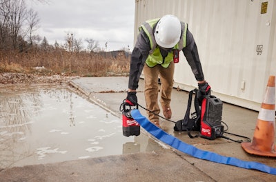 worker with Milwaukee Tool battery-powered submersible pump and backpack console by puddle