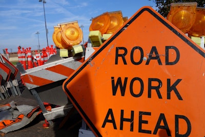 orange road work ahead sign with traffic cones barricades in background