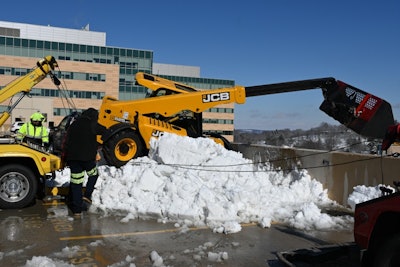 tow truck pulls telehandler to safety after it tipped over top of parking garage