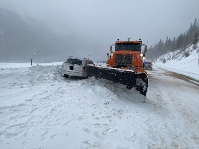 silver jeep cherokee in snow bank beside orange snowplow on highway 40