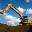 Cat 320 excavator dumping dirt beside hole