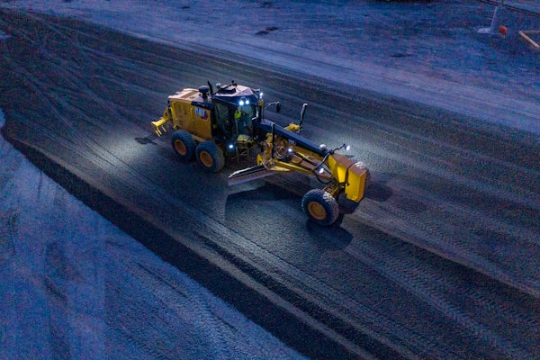 Cat 150 motor grader scraping snow on road at night