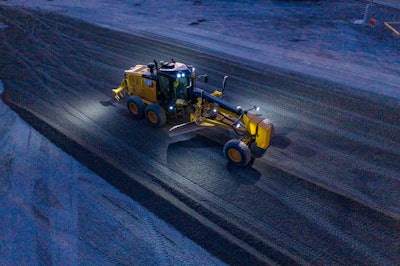 Cat 150 motor grader scraping snow on road at night