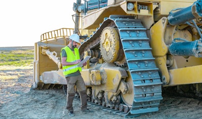 Construction worker using a tablet next to a large bulldozer