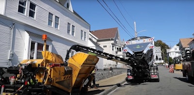 CanAmerican SoilKing Extreme Stone Spreader feeds asphalt to a Weiler paver