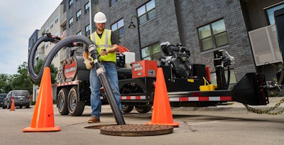 worker holding hose on Ditch Witch HX40G hydro-excavator over manhole