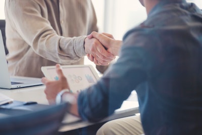Two people shaking hands over a laptop