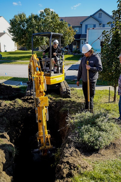 Kato HD35V5 excavator digging ditch beside worker with shovel