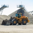 a wheel loader sits by several large stockpiles