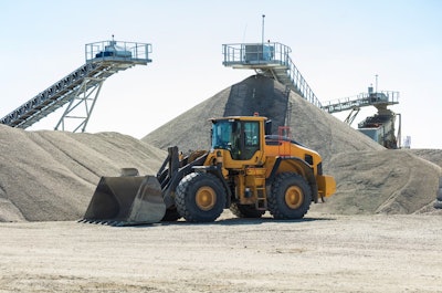 a wheel loader sits by several large stockpiles
