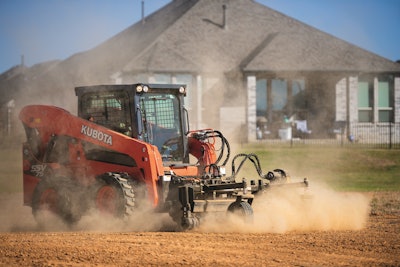 Kubota SSV75 skid steer grading dirt lot in front of house