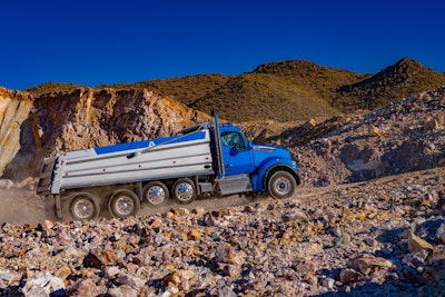 blue Kenworth dump truck with t880s performance hood driving up quarry road