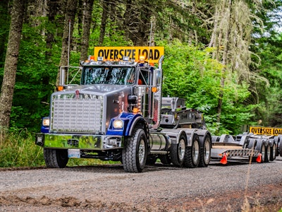 blue Kenworth T800W with oversized load sign empty trailer on forest road