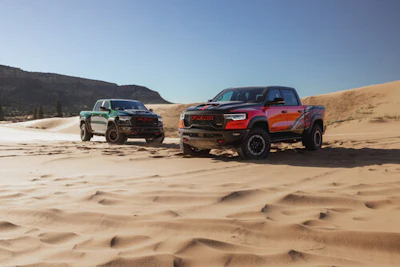 Two rugged pickup trucks on sandy desert terrain with mountains in background