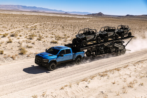 Blue pickup truck towing multiple black off-road vehicles across desert landscape