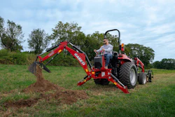 Red CASE IH backhoe loader with operator digging in green pasture field