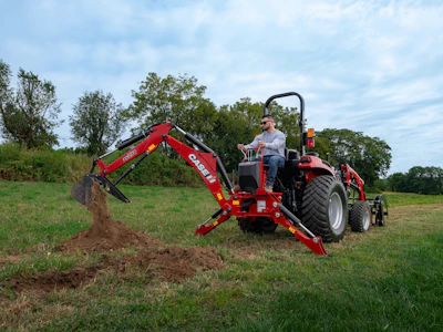 Red CASE IH backhoe loader with operator digging in green pasture field