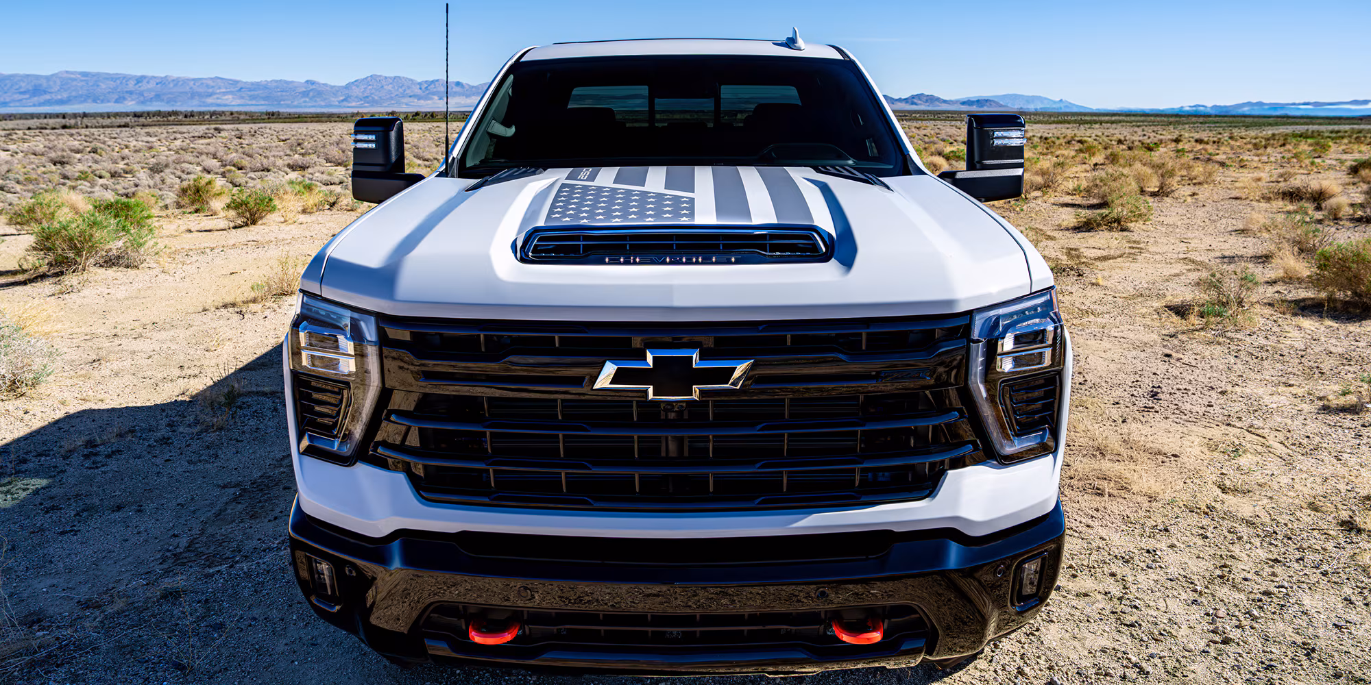 White Chevrolet heavy-duty pickup truck with American flag hood graphic, parked in a desert landscape