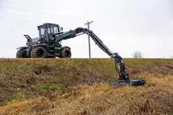 Green and black logging excavator positioned on grassy terrain with extended mechanical arm
