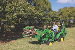 Green John Deere tractor moving logs in grassy field with trees