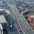 Aerial view of a multi-lane highway interchange with vehicles crossing elevated concrete bridges above an urban cityscape
