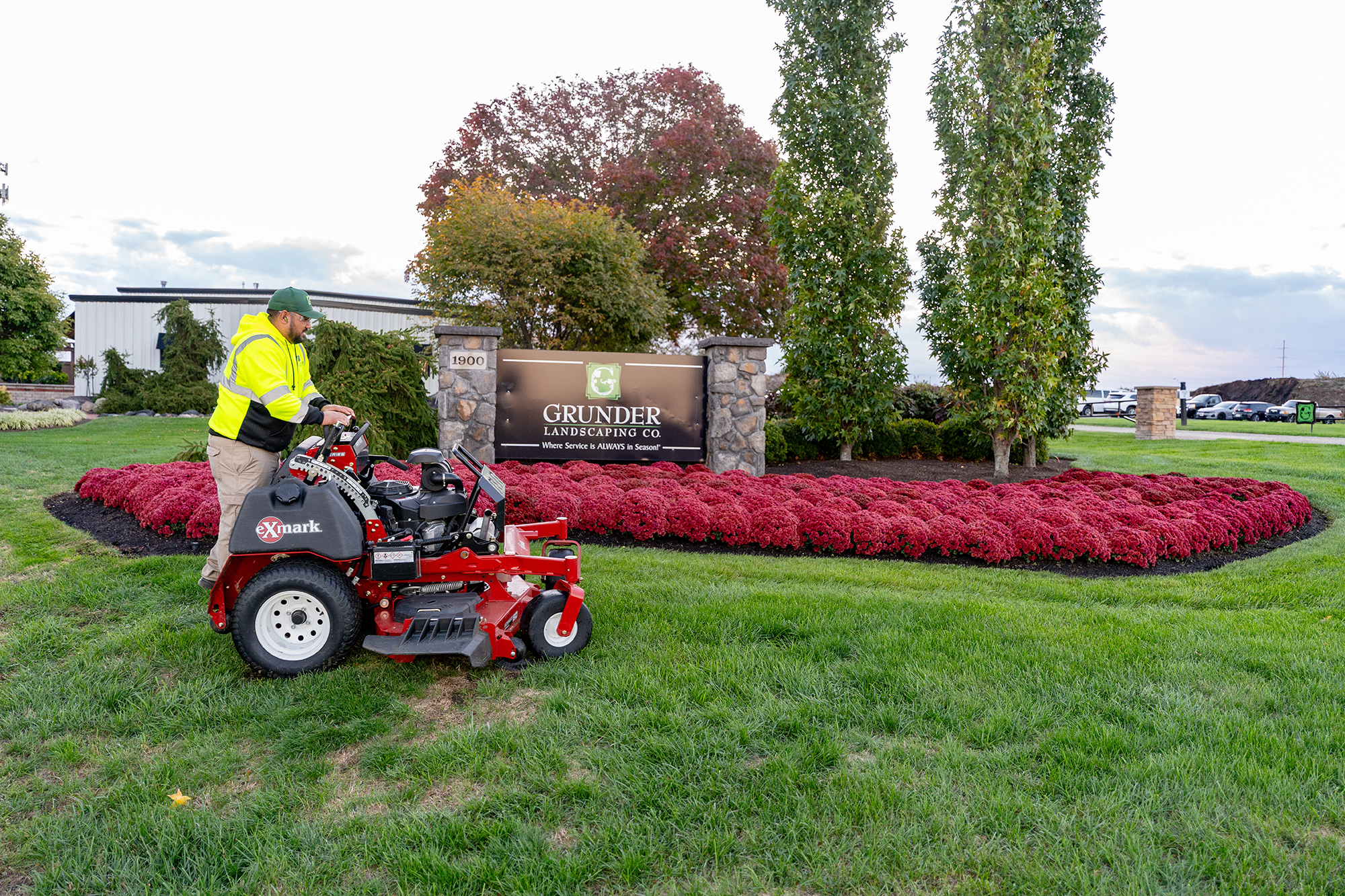 Grunder Landscaping zero-turn mower on green lawn near company sign with red flower beds