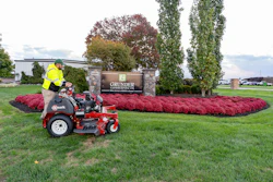 Grunder Landscaping zero-turn mower on green lawn near company sign with red flower beds