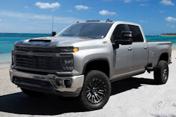 Silver Chevrolet Silverado pickup truck parked on sandy beach with turquoise ocean water in background