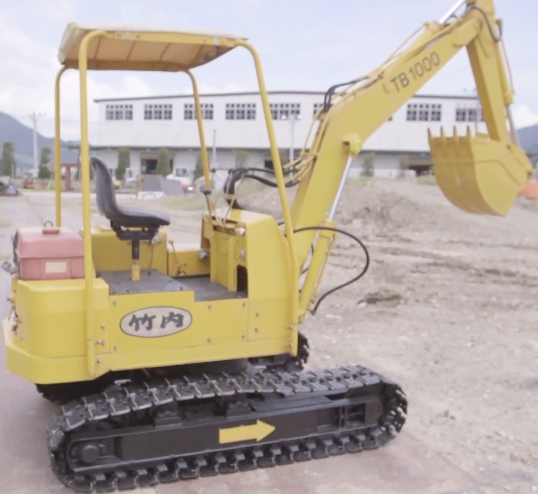 Yellow mini excavator with canopy on construction site with buildings in background
